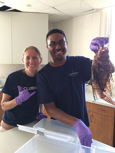 two people pose for a photo, one of them holds up a lionfish