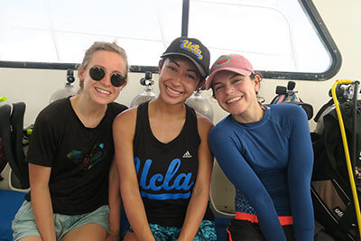 three women pose for a photo surrounded by scuba tanks