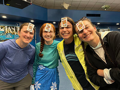 4 women with playing cards stuck to their foreheads