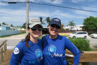 two women wearing earth is blue shirts pose for a photo on a dock