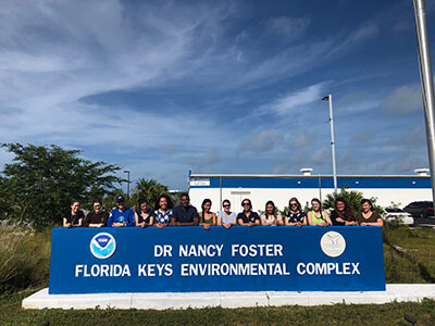 people pose for a photo with the sign for the dr nancy foster florida keys environmental complex
