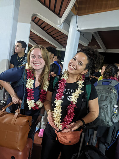 two women pose for a photo while holding luggage