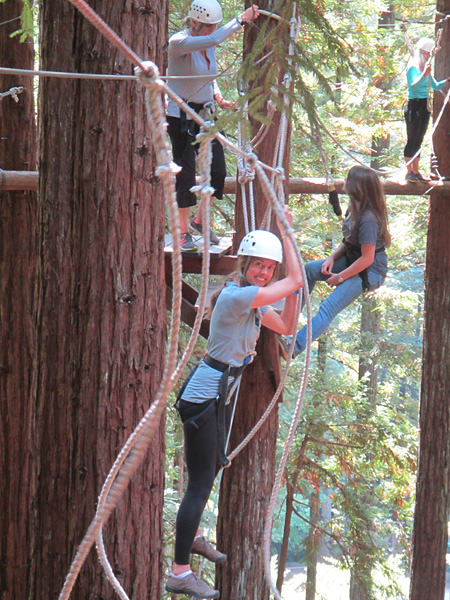Melinda Conners crossing a rope line among the tree tops.